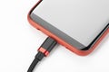 Mobile phone in a red case with a connected cable for charging power on a white background Royalty Free Stock Photo