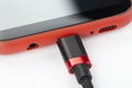 Mobile phone in a red case with a connected cable for charging power on a white background Royalty Free Stock Photo