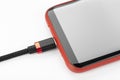 Mobile phone in a red case with a connected cable for charging power on a white background Royalty Free Stock Photo
