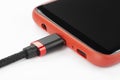 Mobile phone in a red case with a connected cable for charging power on a white background Royalty Free Stock Photo