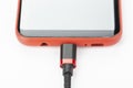 Mobile phone in a red case with a connected cable for charging power on a white background Royalty Free Stock Photo