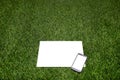 Mobile phone and sheet of paper lying on the grass Royalty Free Stock Photo