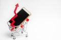 Mobile phone in a supermarket trolley and a red arrow up. high demand for the purchase of a smartphone. online store. consumer cre Royalty Free Stock Photo
