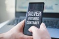 Mobile phone with text: silver futures contract and money, dollars in hand. Financial trading. Investment in precious metals.