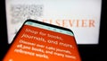 Mobile phone with webpage of academic publishing company Elsevier on screen in front of business logo.