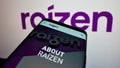 Mobile phone with webpage of Brazilian energy company Raizen S.A. on screen in front of business logo.