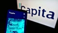 Mobile phone with website of British process outsourcing company Capita plc on screen in front of business logo.