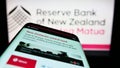 Mobile phone with website of central bank Reserve Bank of New Zealand (RBNZ) on screen in front of logo.