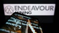 Mobile phone with website of gold exploration company Endeavour Mining plc on screen in front of logo.