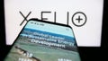 Mobile phone with website of Spanish renewables company X-ELIO Energy S.L. on screen in front of logo.