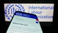 Mobile phone with website of UN agency International Labour Organization (ILO) on screen in front of logo.