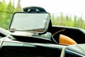 Mobile phone in a weighted clamshell clamp and sunglasses case on dashboard of vehicle with blurred trees in windshield - Soft