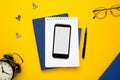 Mobile phone with white notepad , blue notebook and pen on yellow background Royalty Free Stock Photo