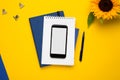 Mobile phone with white notepad , blue notebook and pen on yellow background Royalty Free Stock Photo
