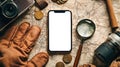 A mobile phone with a white screen is lying on a table with an old map, a magnifying glass, ancient coins and a camera, top view. Royalty Free Stock Photo