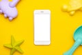 Mobile phone with white screen and plastic beach kid toy on yellow background. The development of fine motor concept Royalty Free Stock Photo