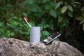 A mobile phone and a white toothbrush with a red shield stand in a plastic glass on a stone Royalty Free Stock Photo