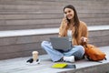 Cheerful young woman sitting outdoors, using laptop, talking on phone Royalty Free Stock Photo