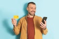 Mobile shopping concept. Happy mature man using smartphone and credit card, making payment over blue studio background Royalty Free Stock Photo