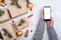 Mobile smart phone with blank screen for app presentation in woman hands, copy space. Christmas gifts wrapped in kraft. Royalty Free Stock Photo