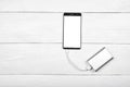 Mobile smart phone with white blank screen charging with power bank battery bank on white wooden desk background, copy space. Royalty Free Stock Photo