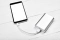 Mobile smart phone with white blank screen charging with power bank battery bank on white wooden desk background, copy space. Royalty Free Stock Photo