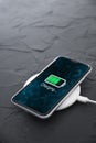 Mobile smart phone on wireless charging device on dark background. Icon battery and charging progress lighting on screen.