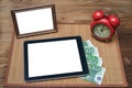 Tablet computer with blank screen, photo frame with copy space and retro style alarm clock and money. Royalty Free Stock Photo