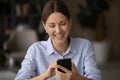 Positive young woman enjoy web surfing on phone at office