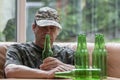 Mobilized soldier in uniform with a bottle of beer in his hand, many empty bottles. Concept: war veteran, family problems,