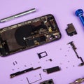 Moblile phone disassembled for battery replacement with screwdrivers on purple bachground