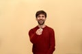 Mock, funny joke. Photo of young man with beard wearing sweater, pointing finger at camera and toothy lough, posing against yellow