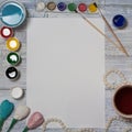 Mock up. Artist workspace on vintage wooden table: watercolor, white paper, paint brushes,water, beads and paper flowers