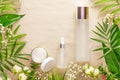 Glass cosmetic bottles, open cream jar, tropic plants and flowers