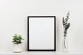 Mock up black frame against white wall with plant and branches on a white shelf Royalty Free Stock Photo