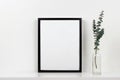Mock up black frame against white wall with vase of branches on a white shelf Royalty Free Stock Photo