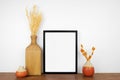 Mock up black frame with autumn branches and decor on a wood shelf