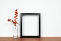 Mock up black frame with fall branches in a vase on a white shelf Royalty Free Stock Photo