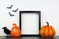 Mock up black frame with Halloween Jack o Lantern, pumpkin and crow decor on a shelf against a white wall Royalty Free Stock Photo