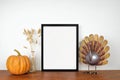 Mock up black frame with thanksgiving turkey, pumpkin and autumn decor on a wood shelf