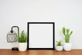 Mock up black square frame with home decor and potted plants wih wood shelf and whitewall Royalty Free Stock Photo