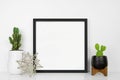 Mock up black square frame with modern home decor on a white shelf against a white wall