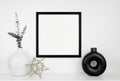 Mock up black square frame with modern home decor on a white shelf against a white wall Royalty Free Stock Photo