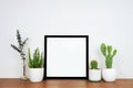 Mock up black square frame with potted plants and decor on a wood shelf against a white wall