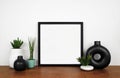 Mock up black square frame with plants and modern circle vase on a wood shelf against a white wall Royalty Free Stock Photo