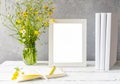 Mock up creation. White frame on white wooden table with grey concrete background, books, notebook and wild flowers Royalty Free Stock Photo