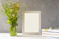 Mock up creation. White frame on white wooden table with grey concrete background, books, notebook and wild flowers Royalty Free Stock Photo