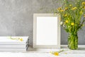 Mock up creation. White frame on white wooden table with grey concrete background, books, notebook and wild flowers Royalty Free Stock Photo