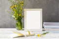 Mock up creation. White frame on wooden table with grey concrete background, books, notebook, pencil and wild flowers Royalty Free Stock Photo