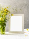 Mock up creation. White frame on white wooden table with grey concrete background and wild spring flowers Royalty Free Stock Photo